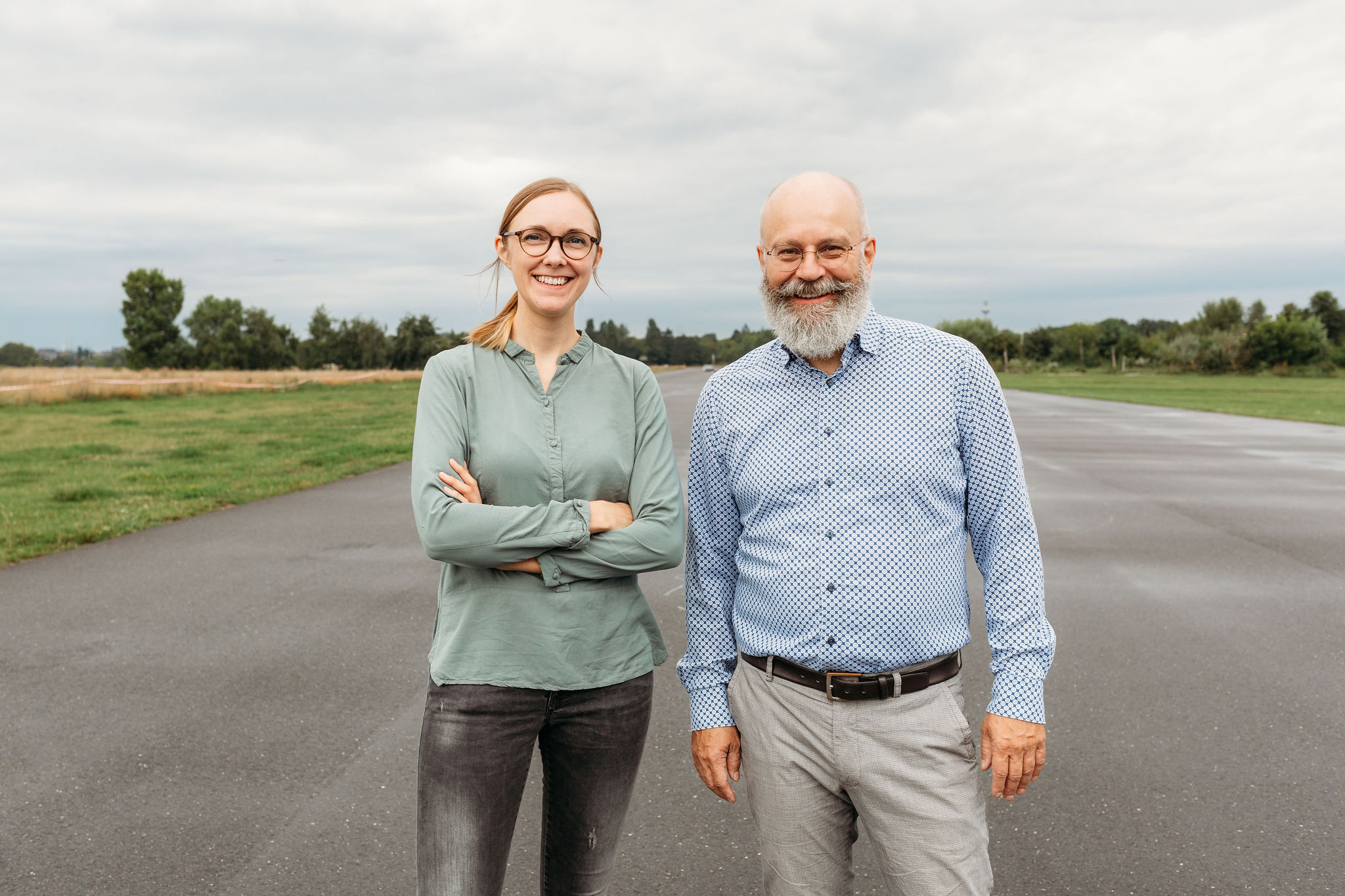 Steph Kunold und Ralf Albers stehen lächelnd nebeneinander auf dem Tempelhofer Feld in Berlin.